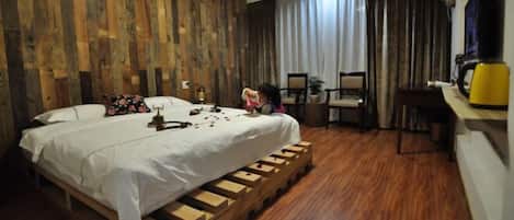 A room with a bed, wooden flooring, a desk, chairs, and a coffee machine.