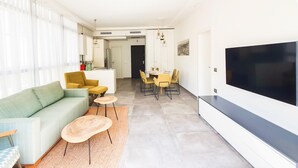 A modern living room with a sofa, coffee table, and TV. There is a dining area with chairs and a table. - Rupin Ruby in Tel Aviv-yafo (Tel Aviv)