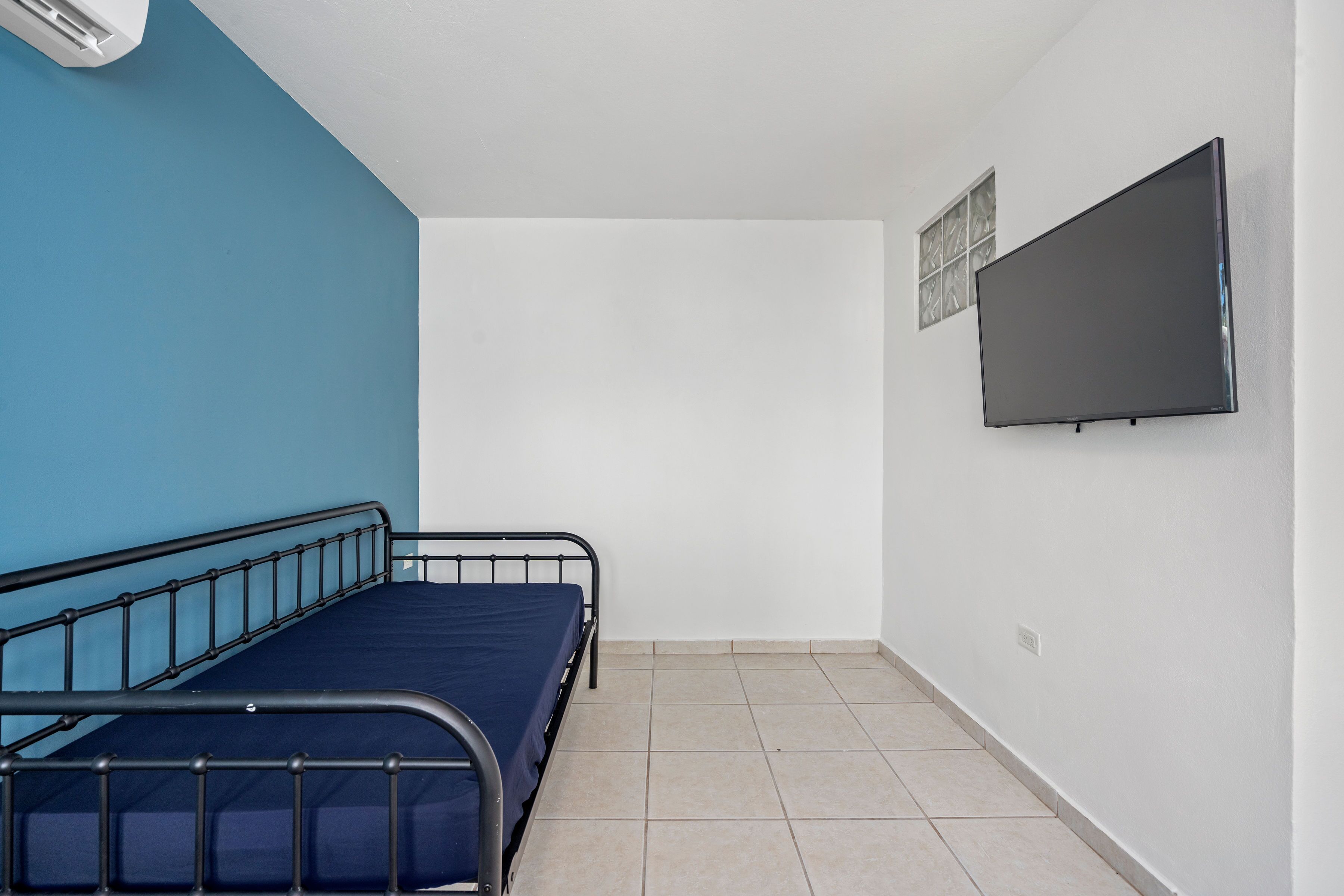 Een kamer met een enkel bed, een wandtv en een raam met zonwering.