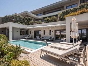 Un área de piscina moderna al aire libre con sillones de descanso y una terraza de madera.