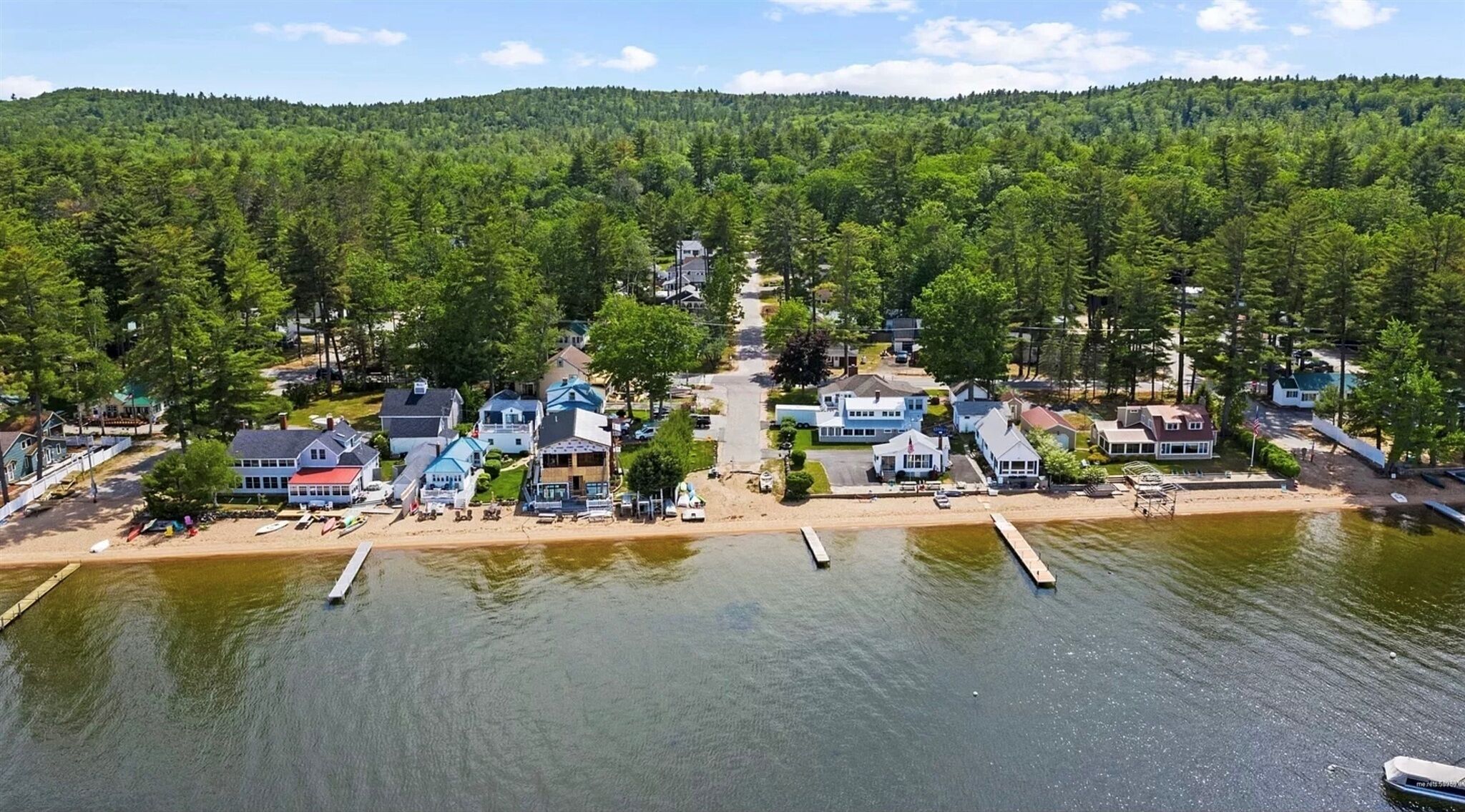 A lakeside community with houses, docks, and a forested hill in the background.