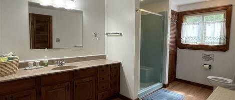 A modern bathroom with a large mirror, wooden cabinets, a sink, and a shower.