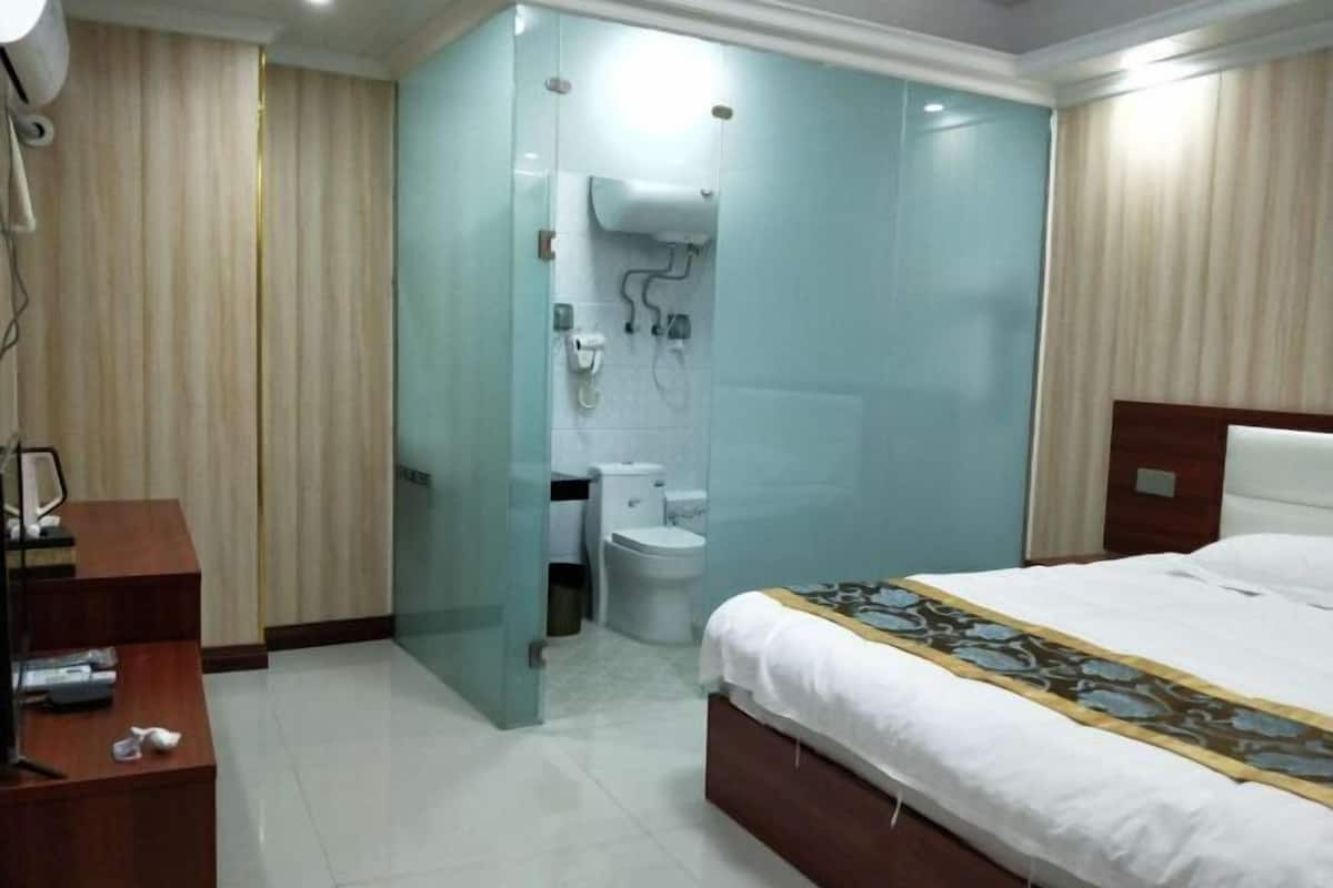 A hotel room with a bed, a desk, a bathroom with a toilet and shower, and a curtain separating the two areas.