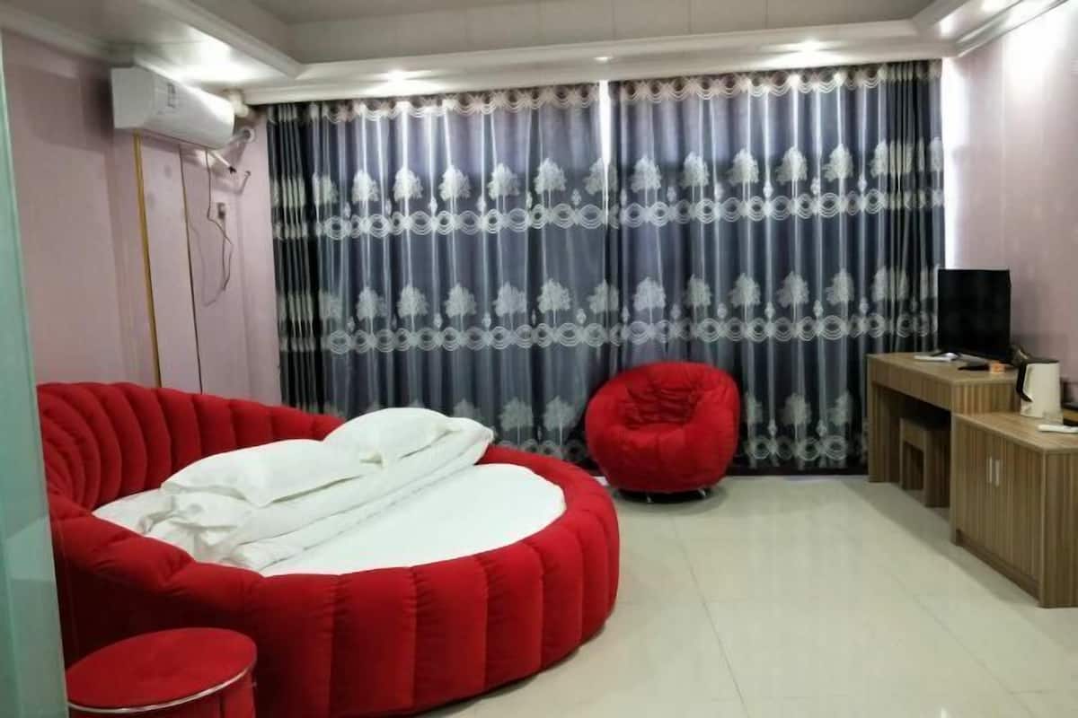 A room with a red sofa bed, a red bean bag chair, a small round table, a TV, and a cabinet.