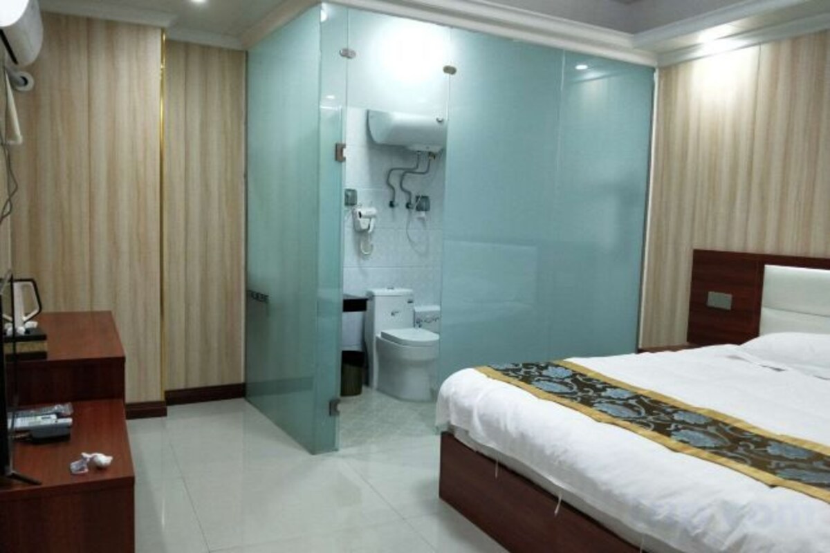 A hotel room with a bed, a desk, a chair, a mirror, a wardrobe, and a bathroom with a toilet and sink.