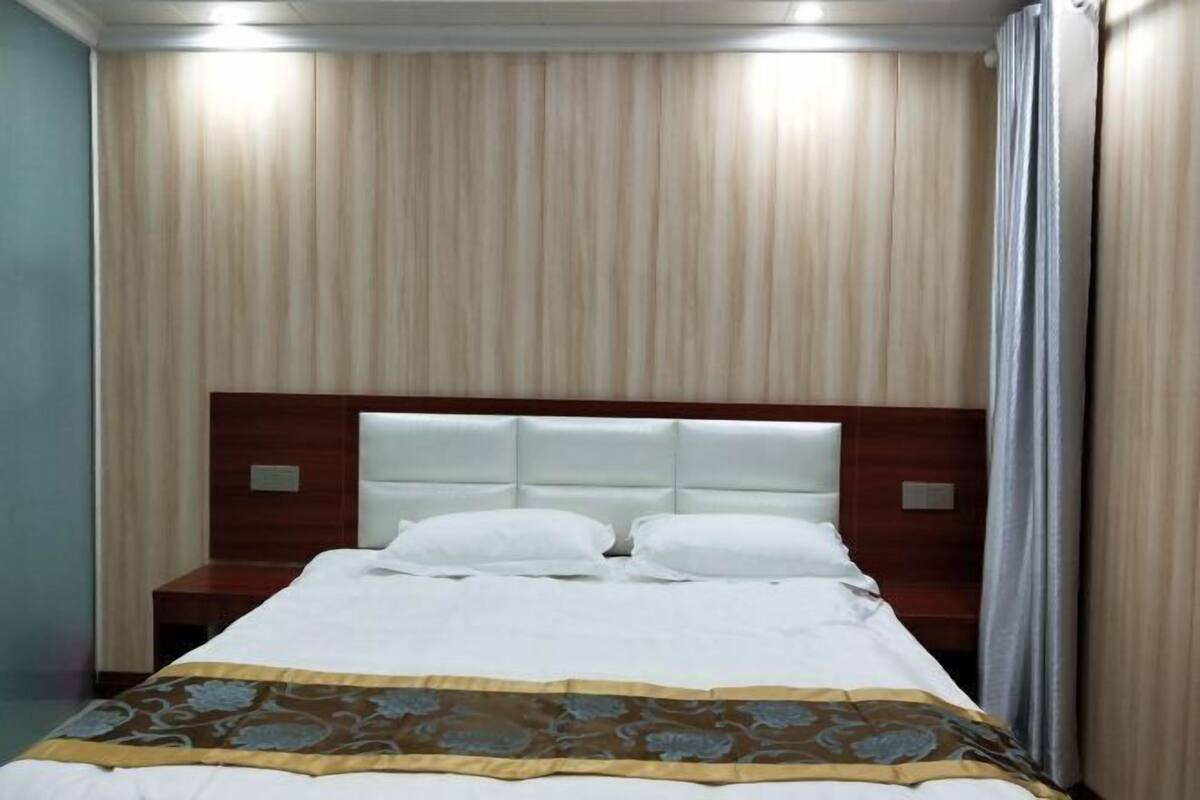A hotel room with a bed, a headboard, a nightstand, and a curtain.