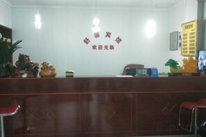 A reception desk with a wooden finish, a wall-mounted sign with Chinese characters, and a potted plant to the left.