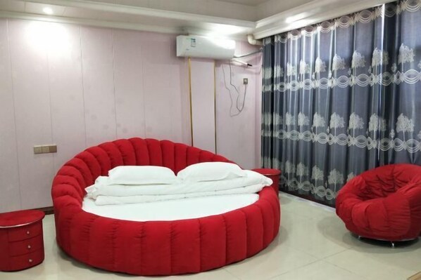 A room with a circular red bed, a red chair, a small red table, and a curtain with a floral pattern.