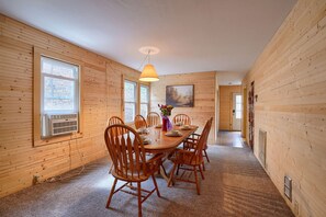 A wooden-paneled room with a dining table set for four, a large window, and a hanging light fixture.
