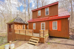 Een houten chalet met een rood dak, een klein terras en een steiger die in het water uitsteken.