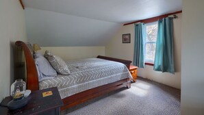 Un dormitorio con una cama de madera, una mesita de noche, una lámpara, una ventana con cortinas y un cuadro pequeño en la pared.
