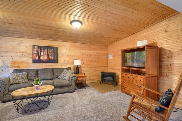 Ein gemütliches Holzblockhaus-Interieur mit einer Couch, einem Holztisch, einem Fernseher, einem Kamin und einem Schaukelstuhl.