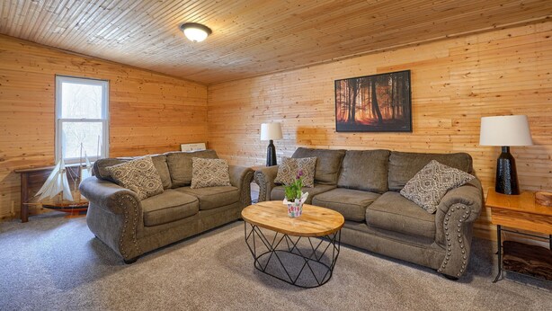 Interior acogedor de una cabaña de troncos con dos sofás, una mesa de centro de madera y una ventana con un modelo de velero.