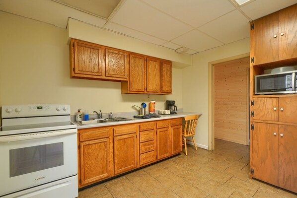A kitchen with wooden cabinets, a white stove, a microwave, and a wooden chair.