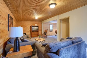 Ein gemütliches Holzhaus-Interieur mit einer Couch, einem Holztisch, einem Schaukelstuhl und einem Fernseher.