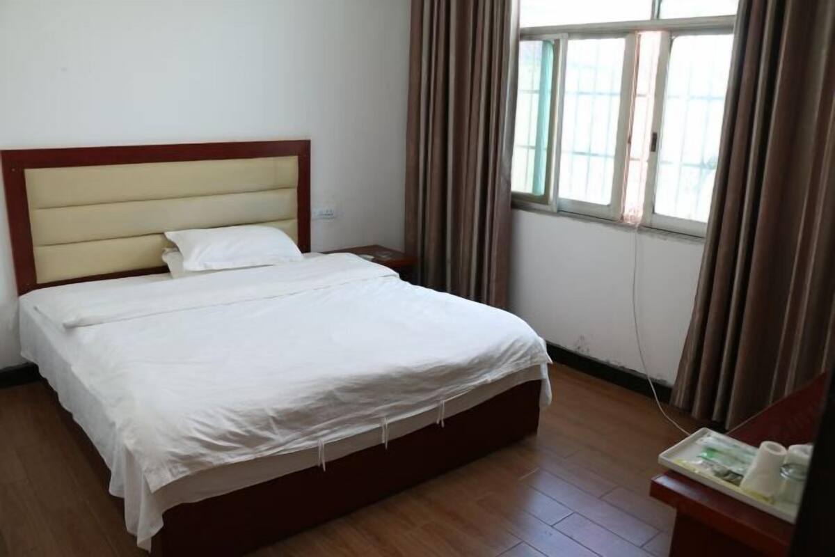 A hotel room with a bed, a nightstand, a window with curtains, and a wooden floor.