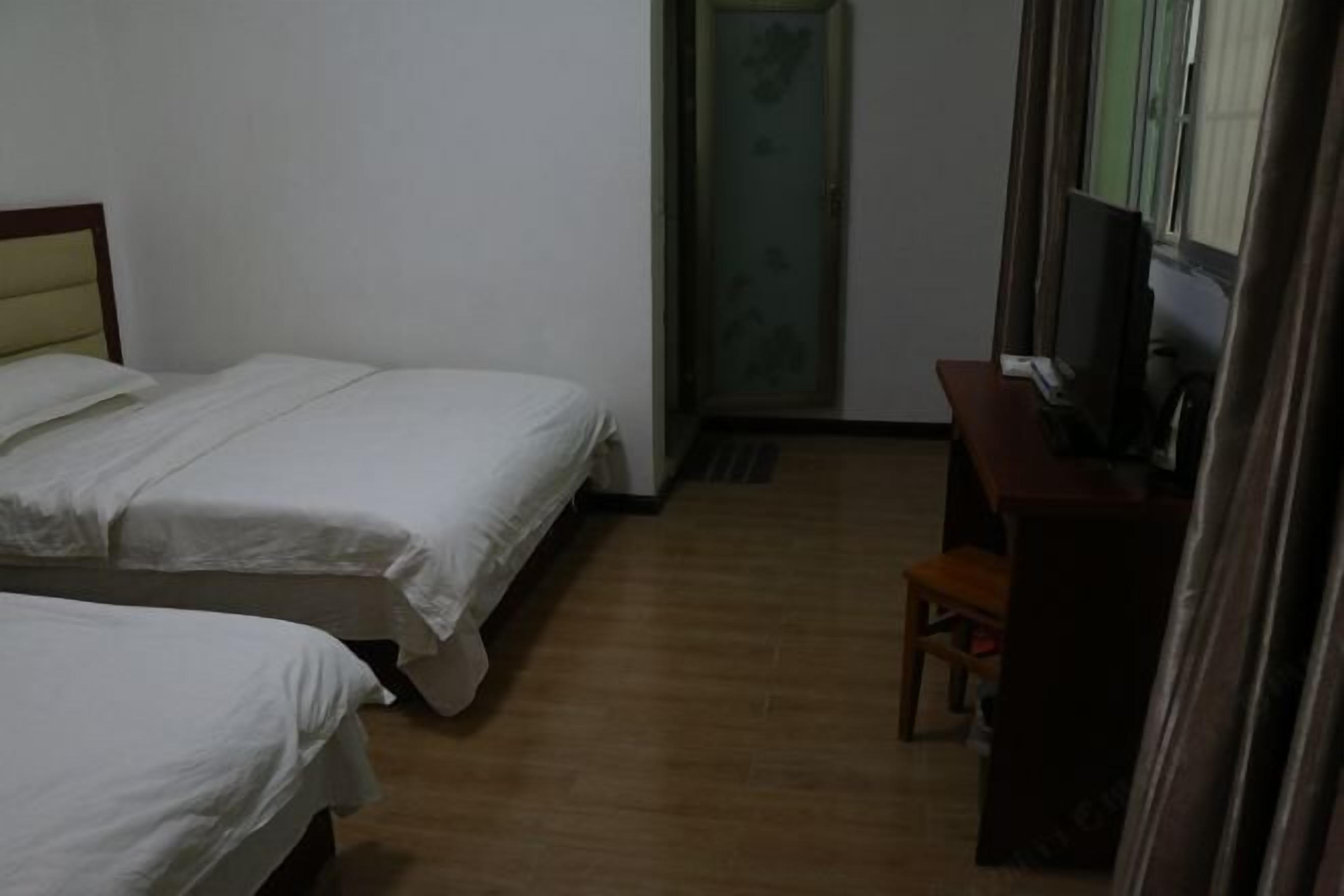 Ein Hotelzimmer mit zwei Betten, einem Schreibtisch mit Fernseher und einem Fenster mit Vorhängen.