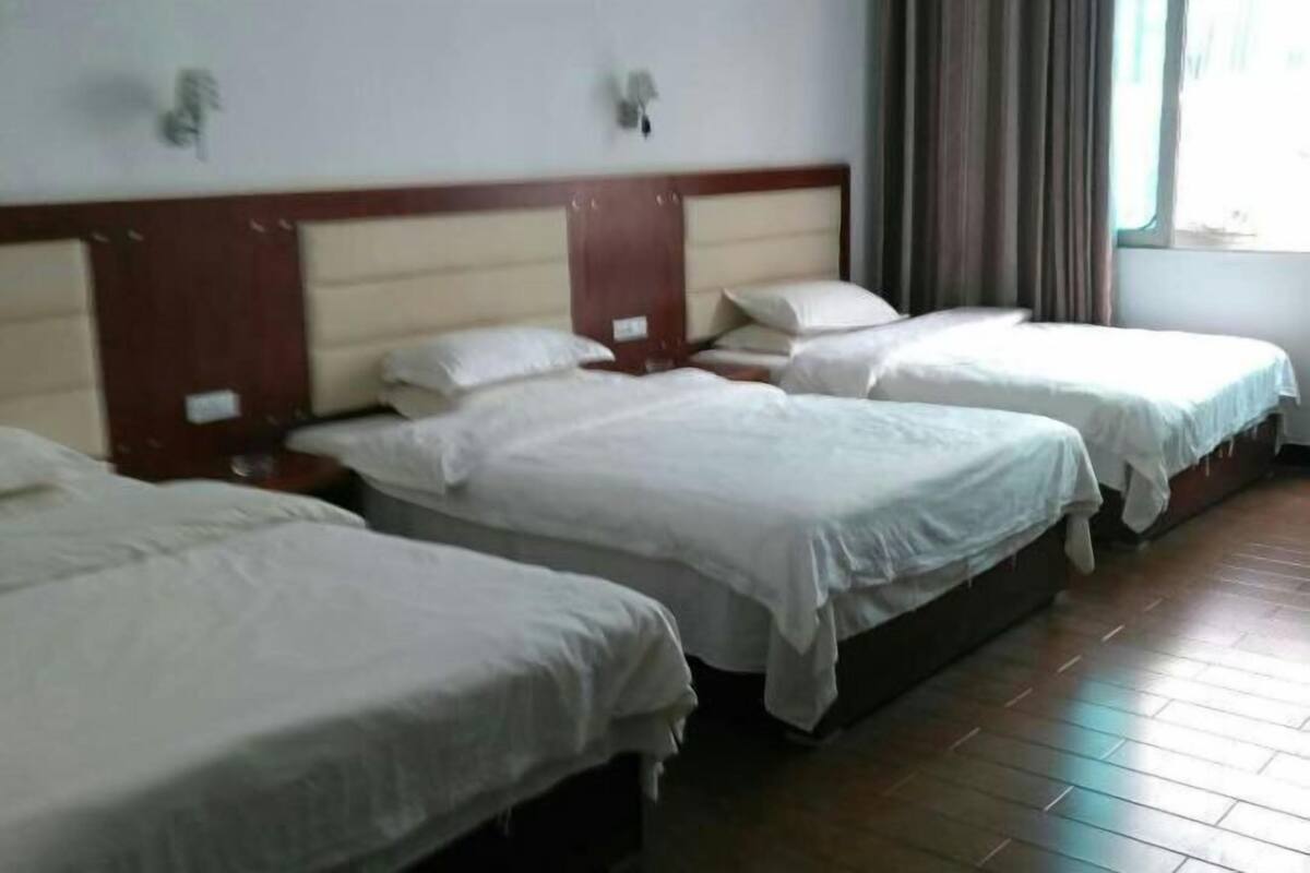 A hotel room with three single beds, wooden headboards, and a large window with curtains.