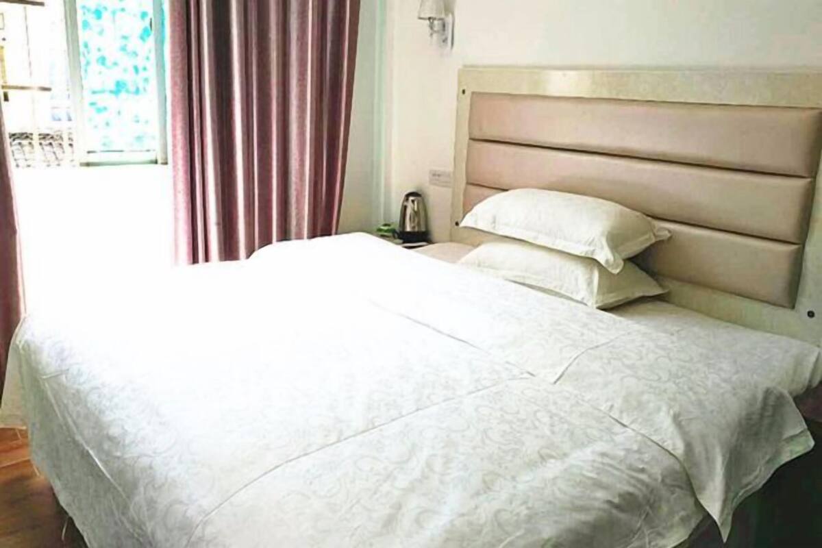 A neatly made bed with a headboard, a bedside table with a lamp, and a window with curtains.