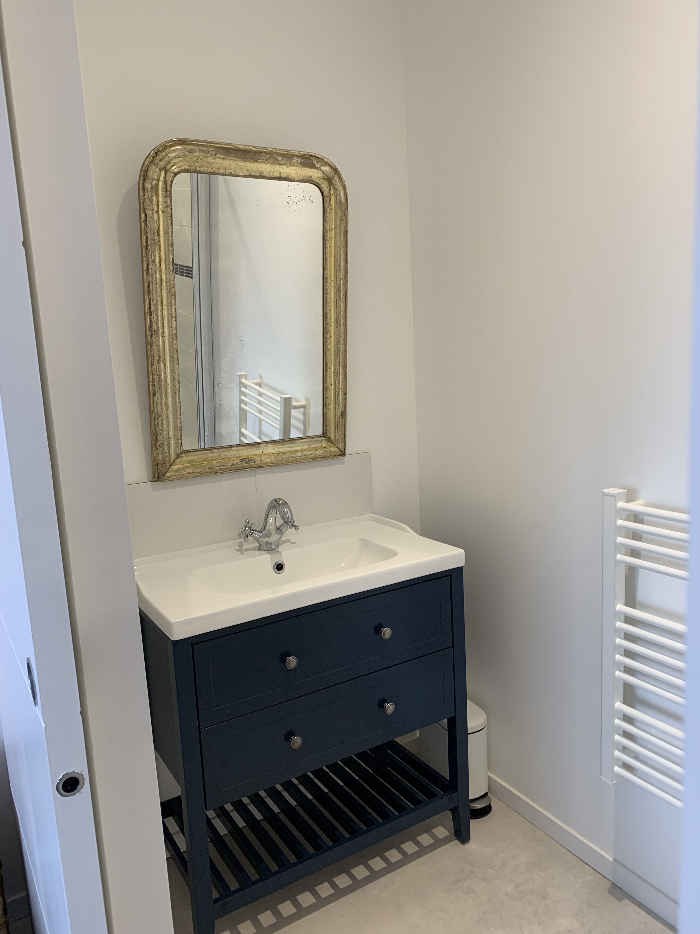 A bathroom with a white sink, dark blue cabinet, and a gold-framed mirror.