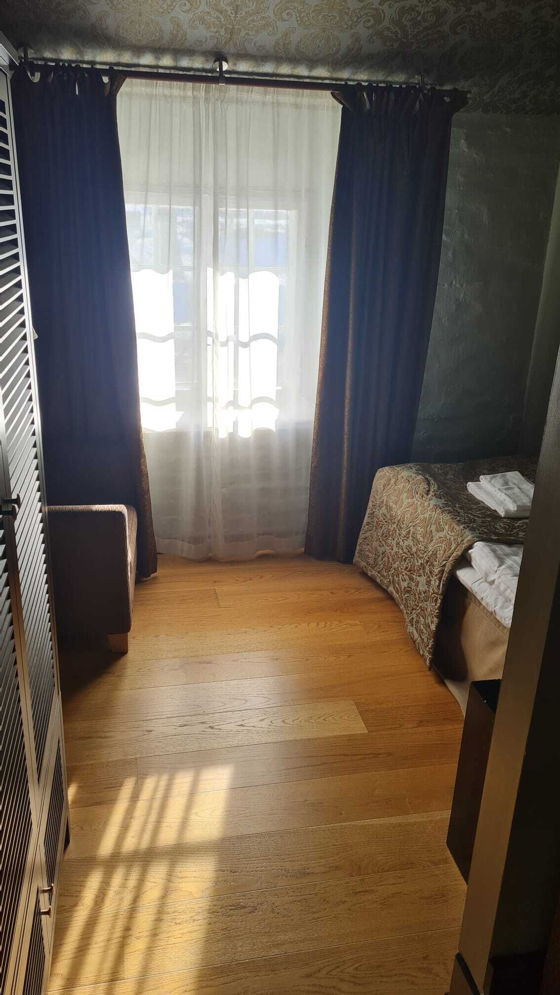 A small, cozy room with a bed, a window with curtains, and a radiator.