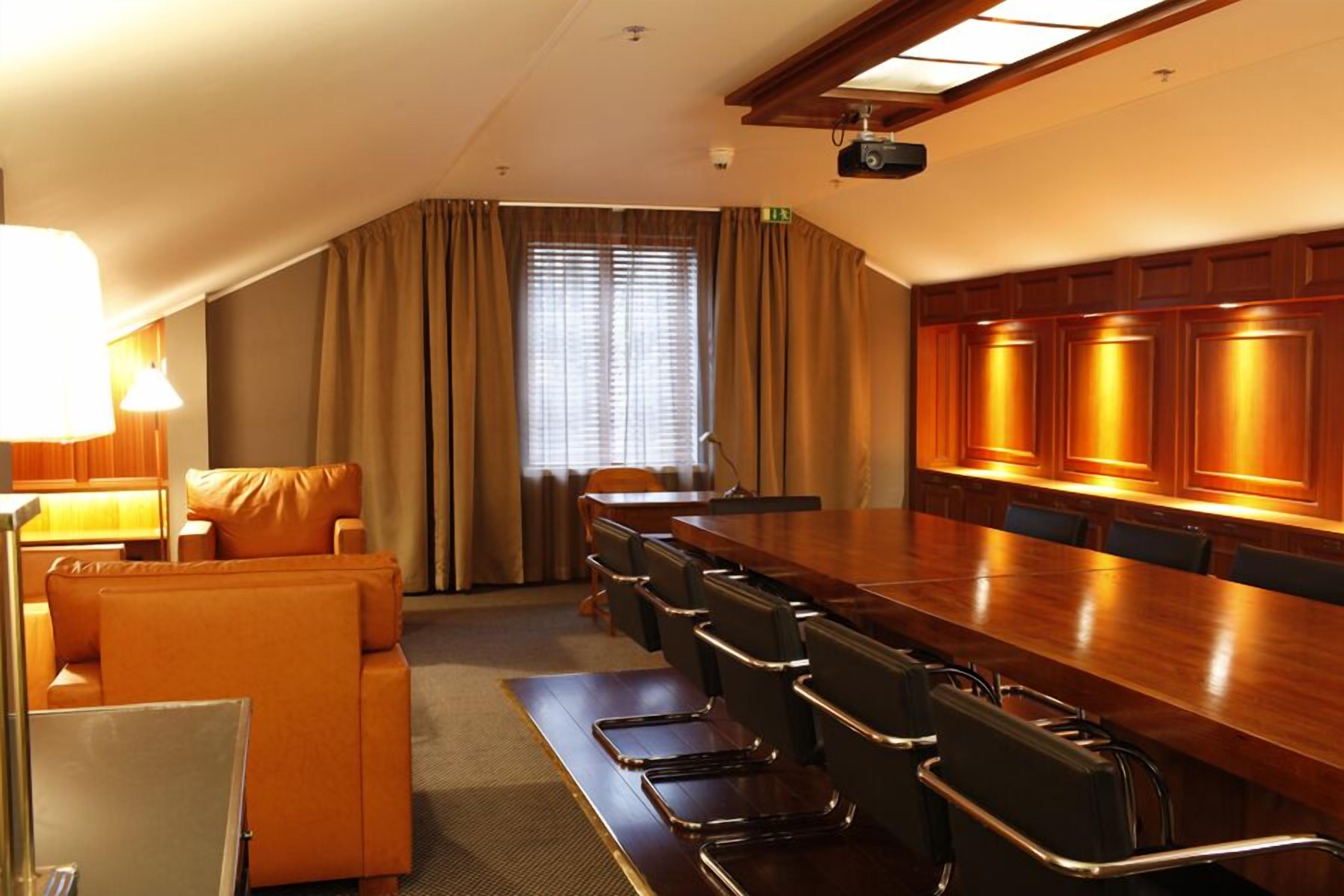 Un salón de conferencias con una mesa larga, sillas, un sofá y un proyector.