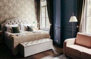 Un dormitorio con una cama de cabecera capitonada, un banco a juego, un sofá rosa y una ventana con cortinas.