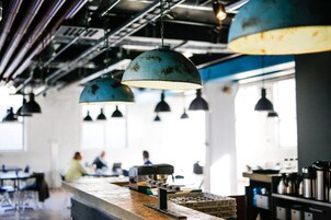 Zona de bar con lámparas azules colgantes, una máquina de café y un mostrador con diversos artículos.