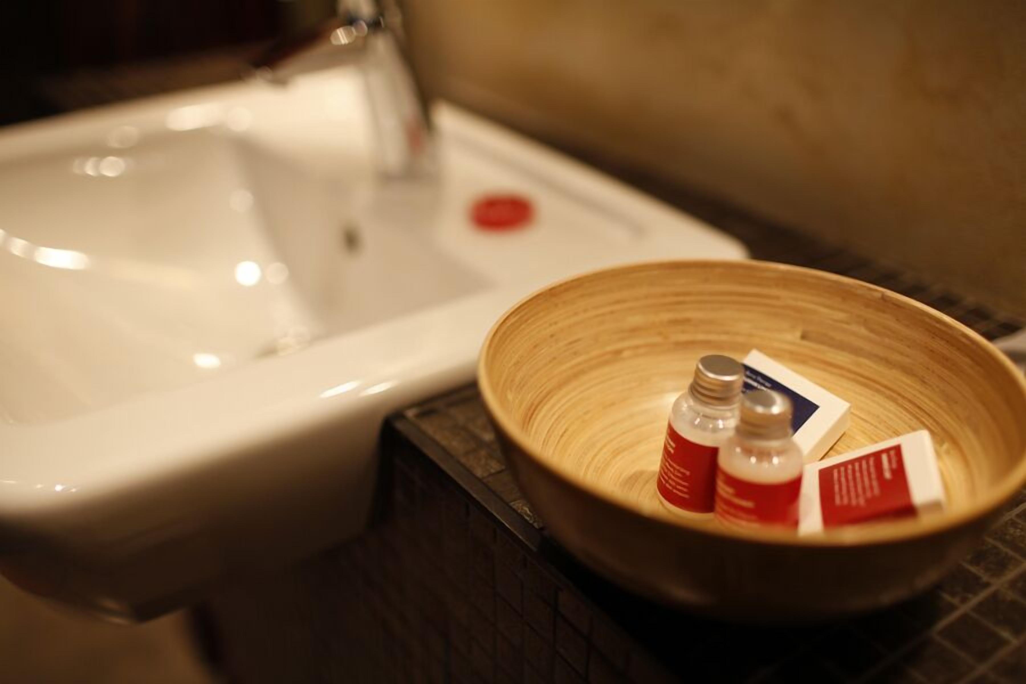 A bathroom sink with a wooden bowl containing toiletries.