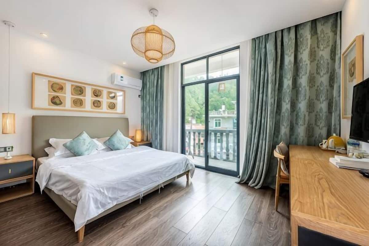 A bedroom with a bed, bedside tables, a desk, and a large window with curtains.
