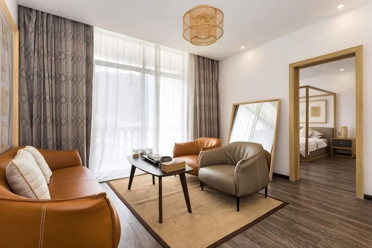 A modern hotel room with a sofa, armchair, coffee table, and a bed with a canopy.