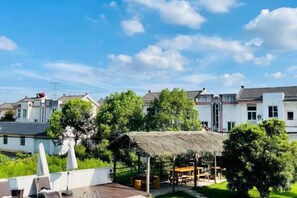 A rooftop terrace with a thatched roof seating area, surrounded by greenery and residential buildings. - Defengju Inn (Deqing)