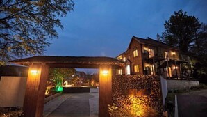 Una entrada bien iluminada con un arco de madera, un muro de piedra y una casa al fondo.