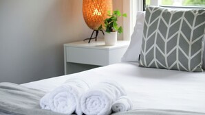 A neatly made bed with rolled white towels, a white bedside table with a potted plant, and a geometric patterned pillow. - 5BR Home w/ Saltwater Pool – Pet Friendly, Near Seacliff Beach & Marion | Ideal for Extended Stays (Seacliff Park)