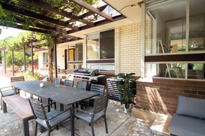 Une terrasse extérieure avec une table à manger, des chaises et un barbecue.