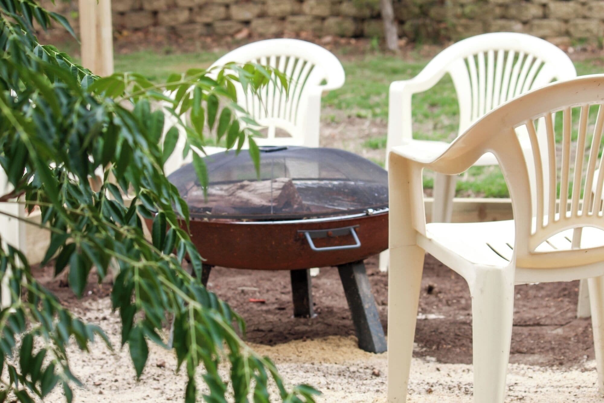 Un barbecue avec une grille en métal, entouré de chaises en plastique blanches.