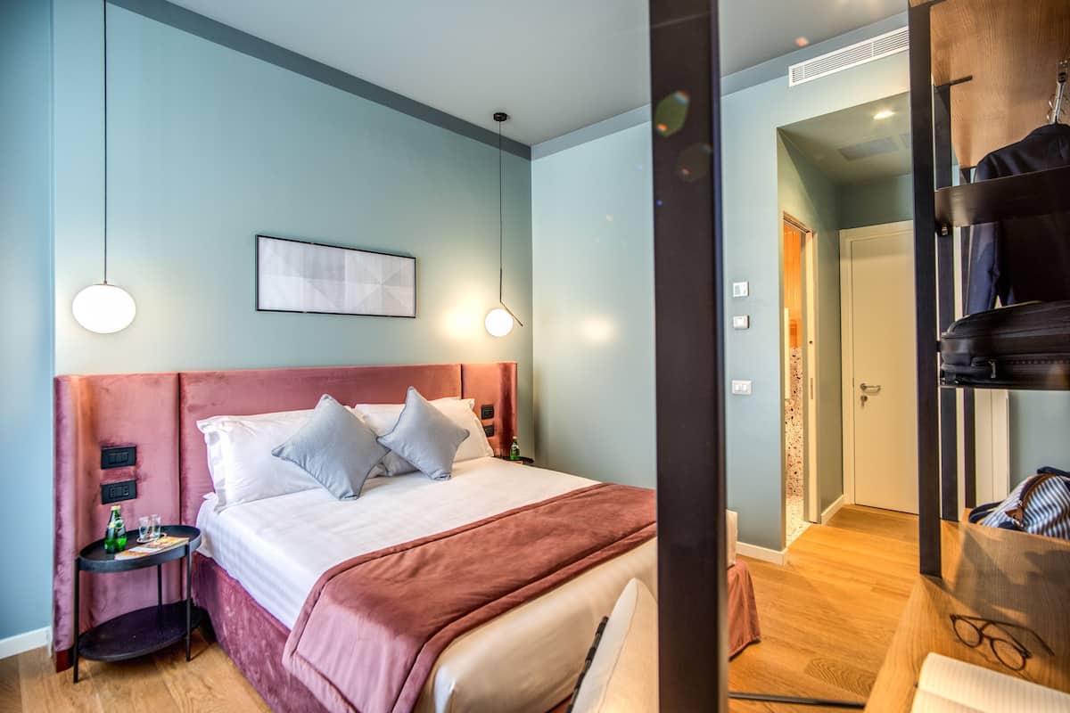 A hotel room with a bed, bedside tables, a wardrobe, and a door leading to another room.