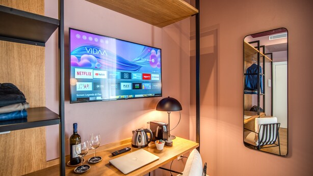 A hotel room with a wooden desk, a flat-screen TV displaying streaming services, a mirror, and a bed with a white pillow. - Sheva Boutique Hotel (Milan)