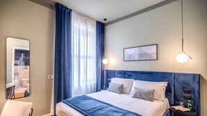 A modern hotel room with a large bed, a side table, a chair, a mirror, and a window with curtains. - Sheva Boutique Hotel (Milan)