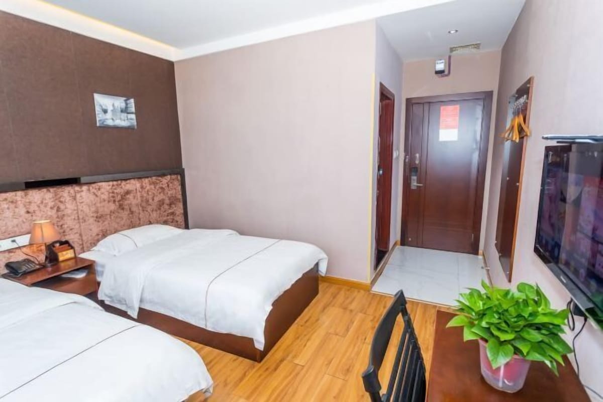 Une chambre d’hôtel avec deux lits, un bureau avec une chaise, une télévision et une plante.