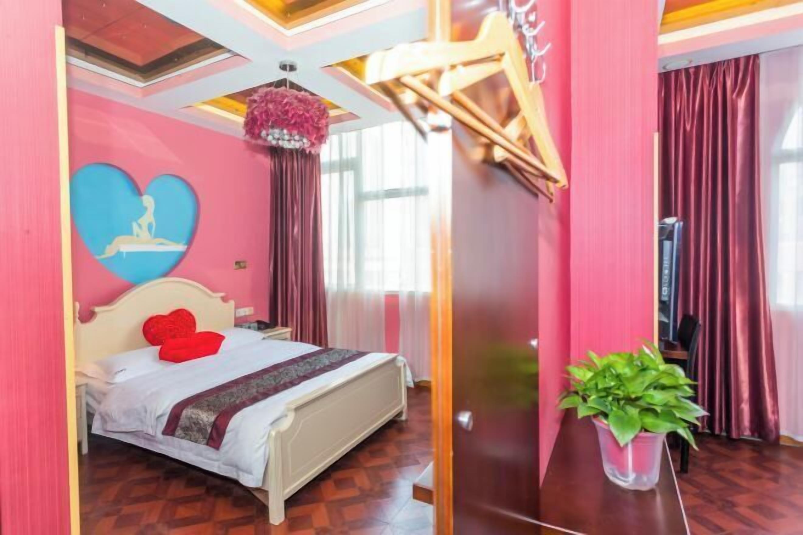 A bedroom with a bed, a heart-shaped wall decoration, a potted plant, and a piano in the corner.