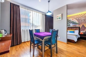Ein Hotelzimmer mit Esstisch, Stühlen, einem Bett und einem Fenster mit Vorhängen.