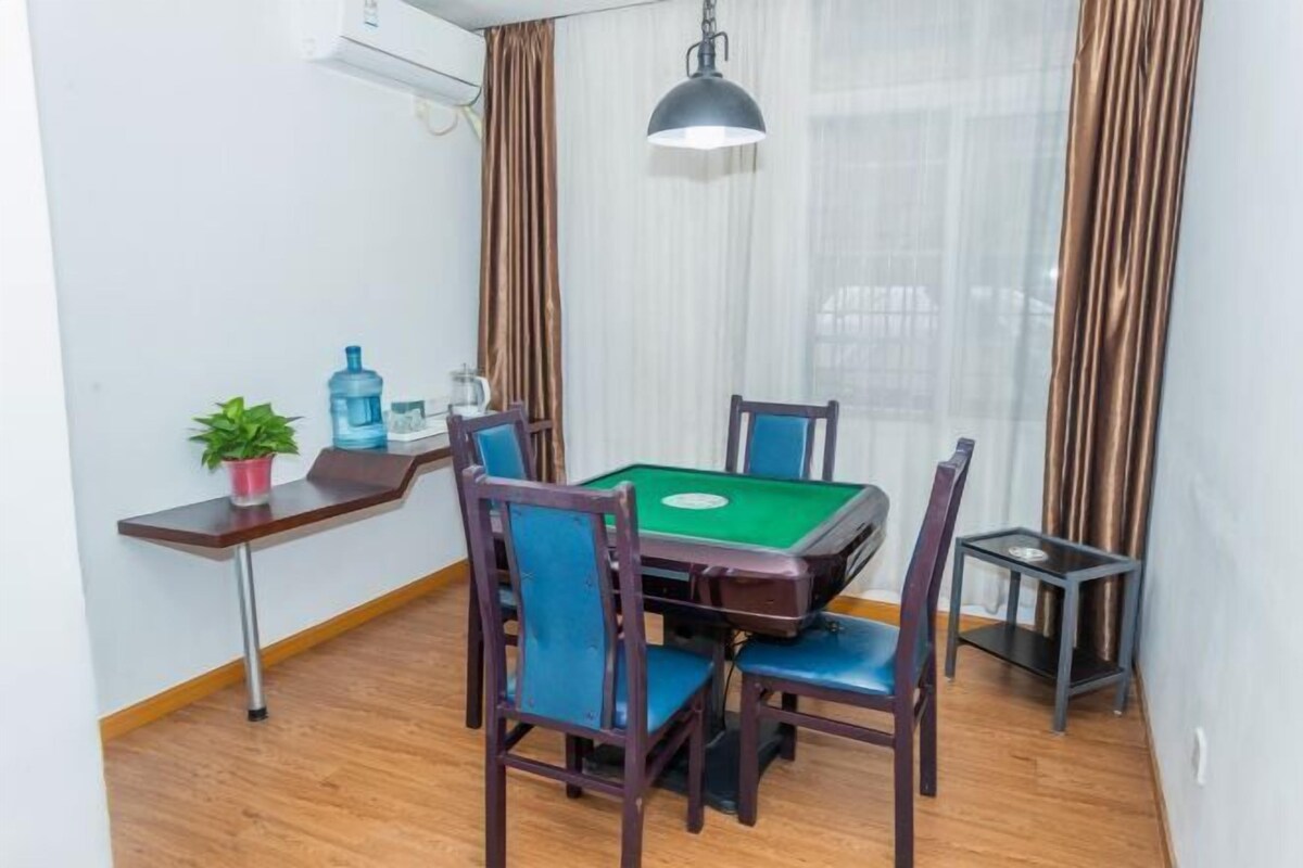 Une pièce comprenant une table de billard verte, quatre chaises, une petite table avec une bouteille d’eau et une plante, ainsi qu’une lampe suspendue.