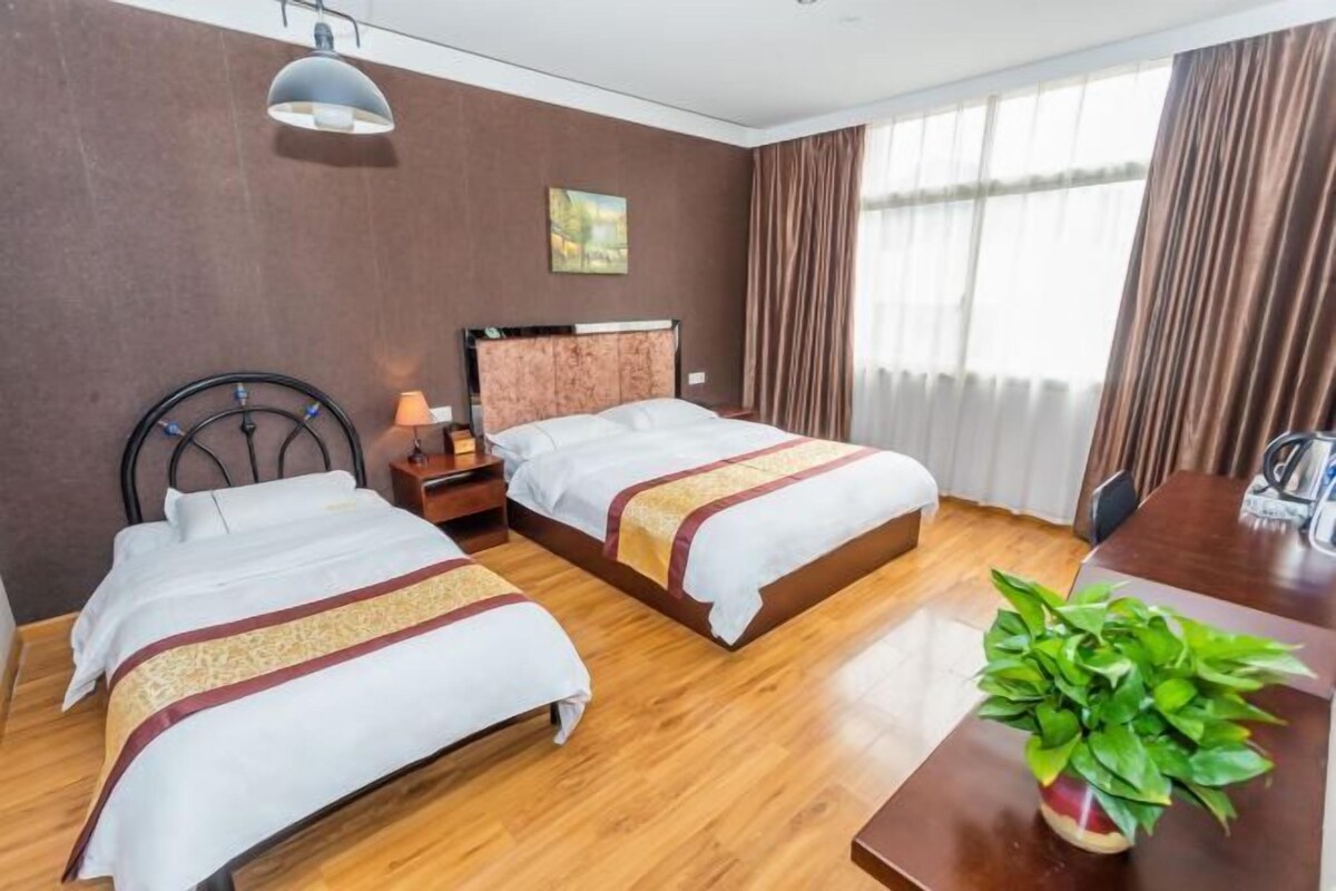 Une chambre d’hôtel avec deux lits, un plancher en bois, un bureau avec une plante et un tableau au mur.