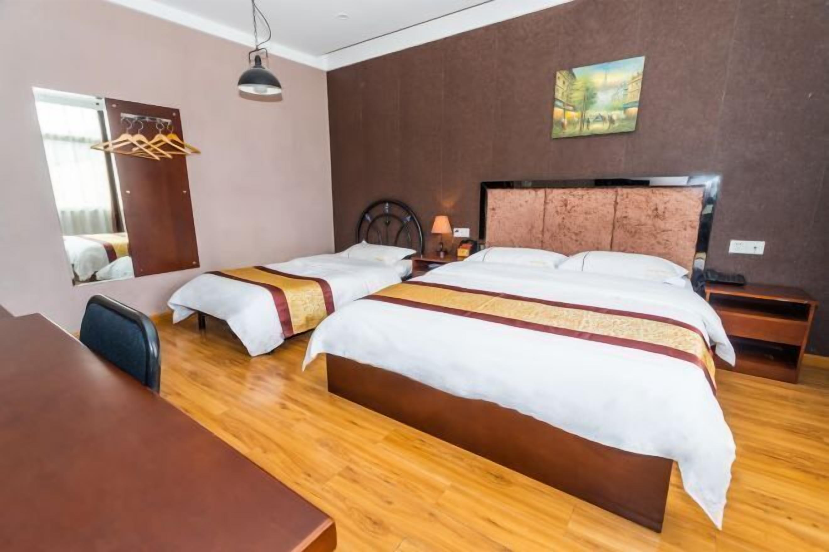 A hotel room with two beds, a wooden desk, a mirror, a hanging light, and a painting on the wall.