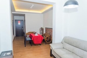 Un salon moderne avec un canapé, une table à manger recouverte d’une nappe rouge et un fauteuil roulant ancien.