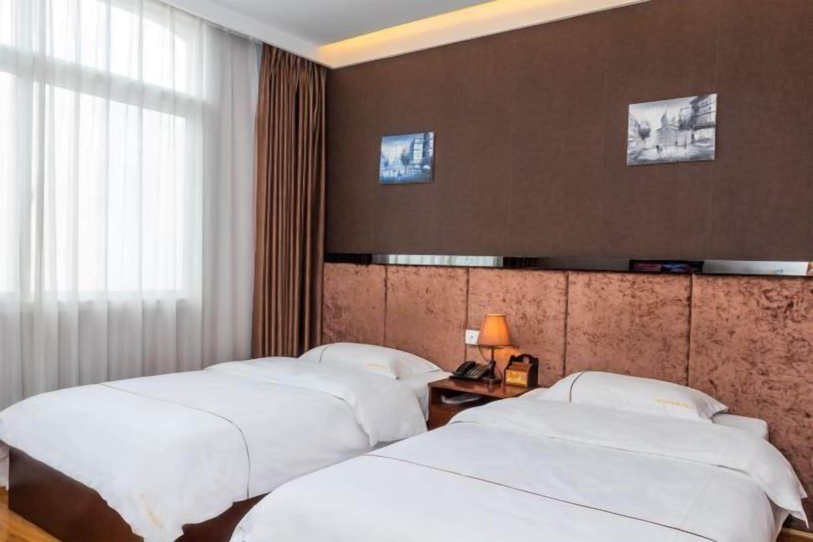 Een hotelkamer met twee bedden, een nachtkastje met een lamp en twee ingekaderde foto’s aan de muur.