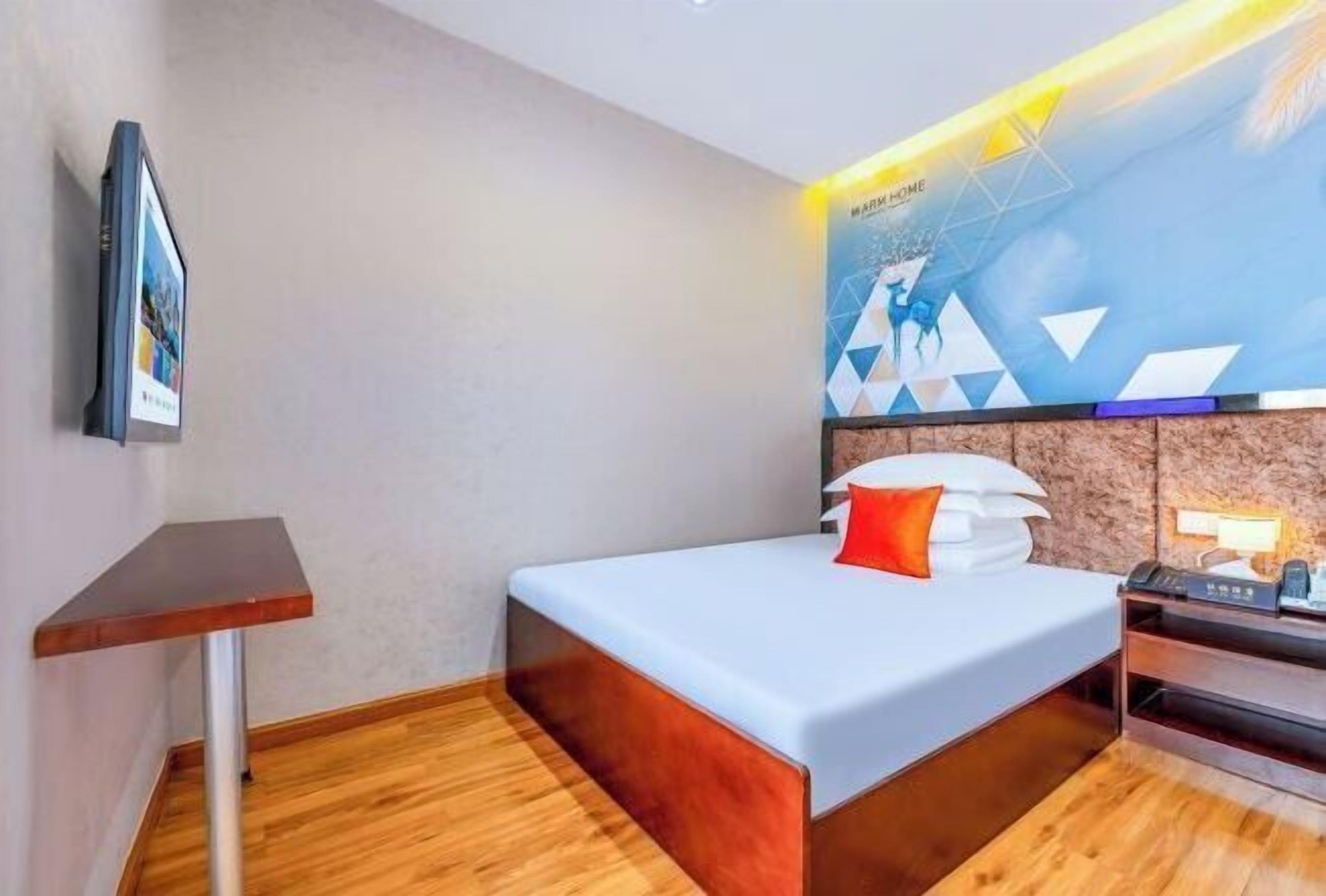 A modern hotel room with a bed, a desk, and a wall-mounted TV.