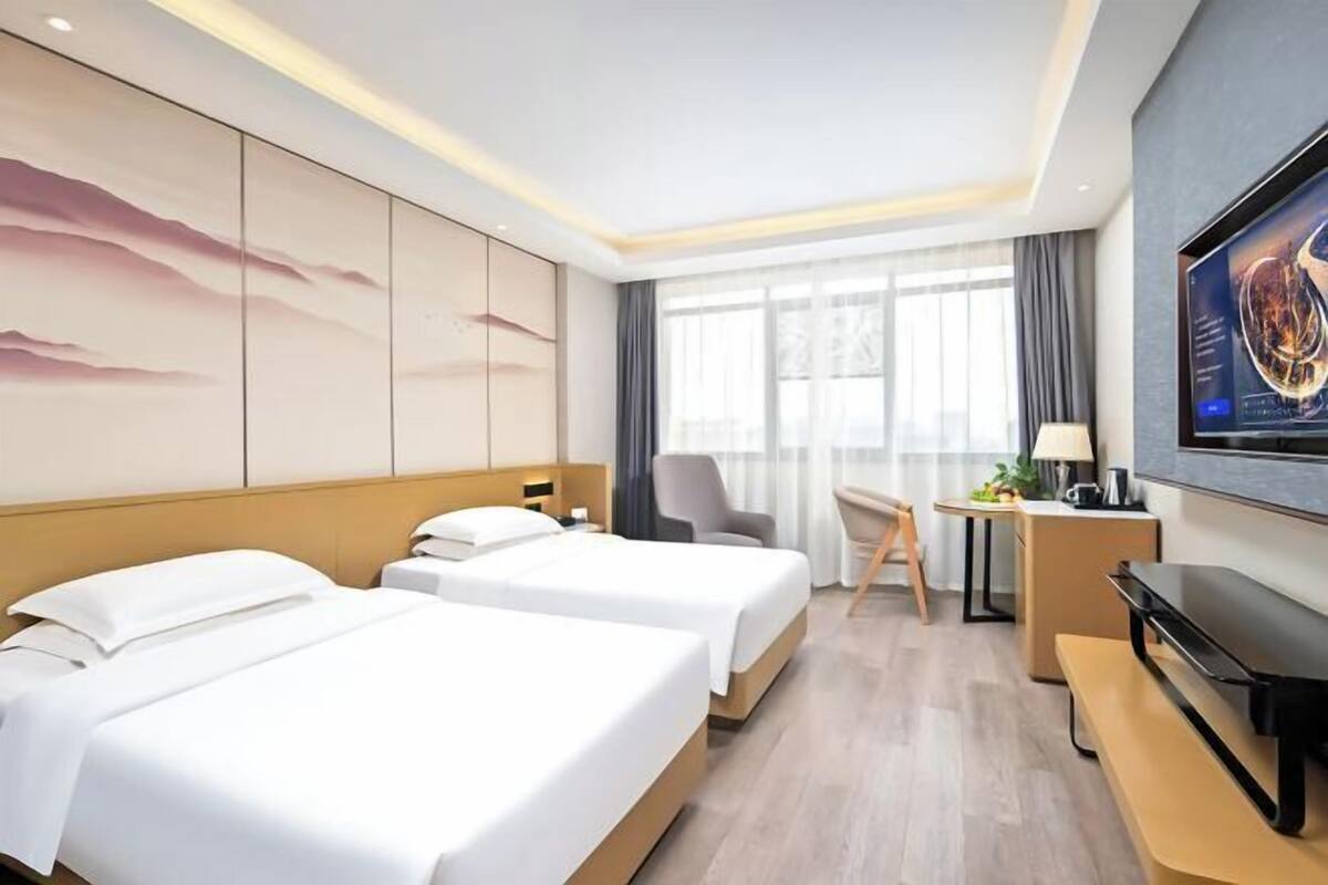 A hotel room with two beds, a desk, a chair, a TV, and a large window.