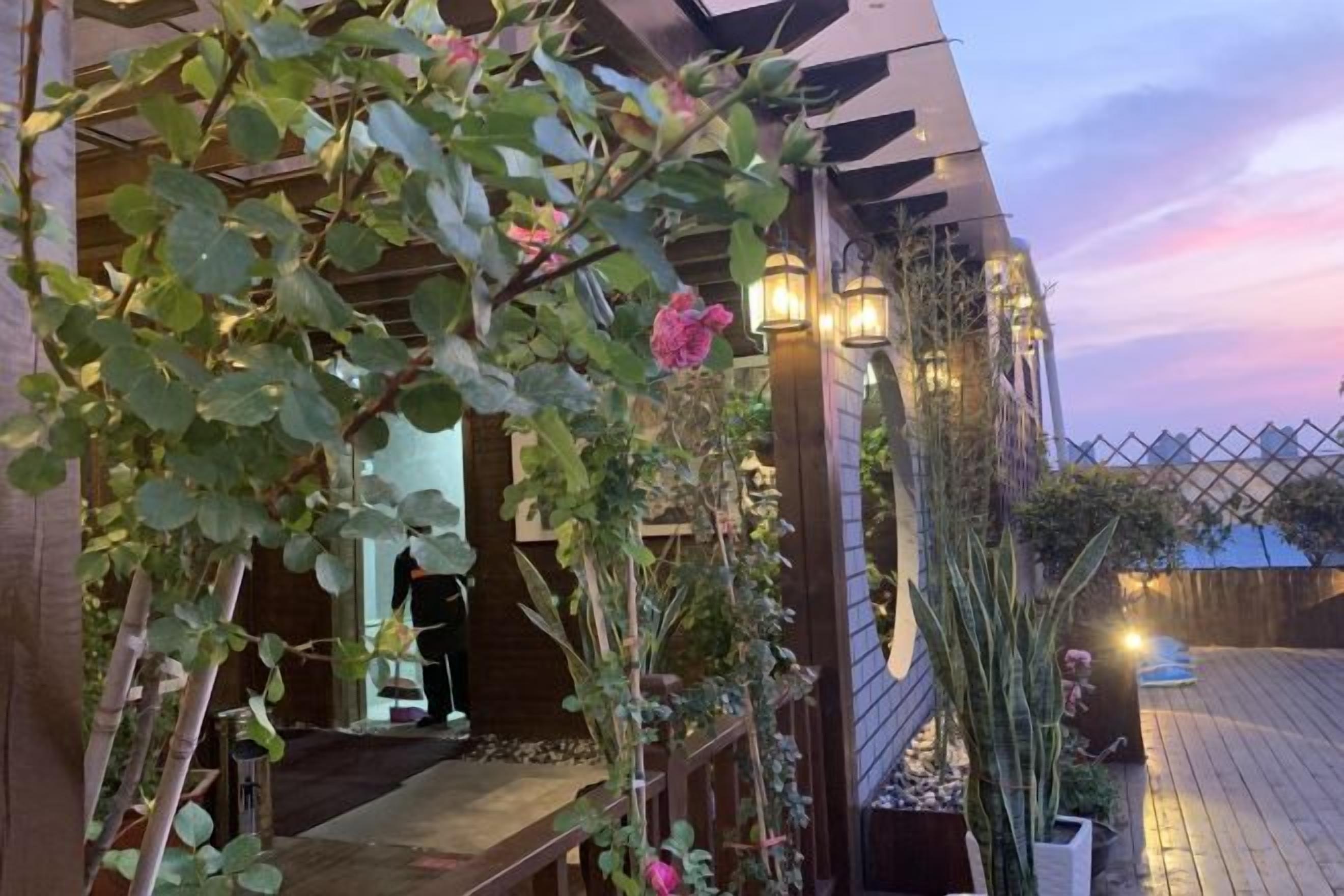 En træterrasse med et pergola, plantekasser og udsigt til en bygning i baggrunden.